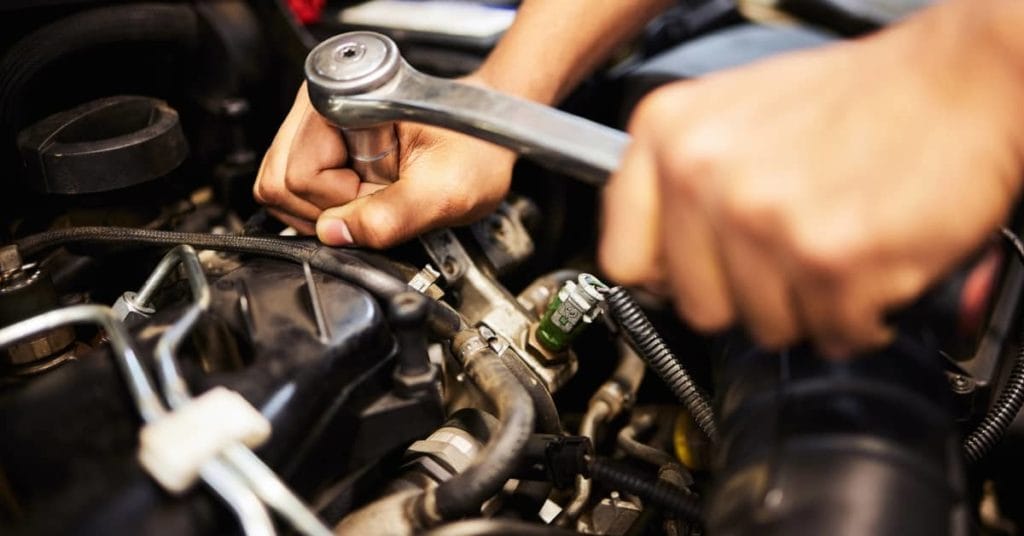 A mechanic uses a wrench to tighten a component in a car's engine, demonstrating vehicle maintenance and repair expertise.