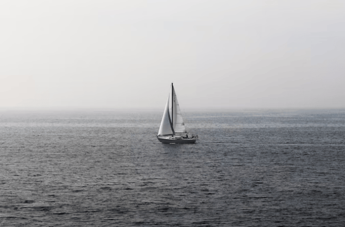 Sailboat glides across a calm, misty sea, showcasing a tranquil maritime scene ideal for promoting relaxation and adventure.