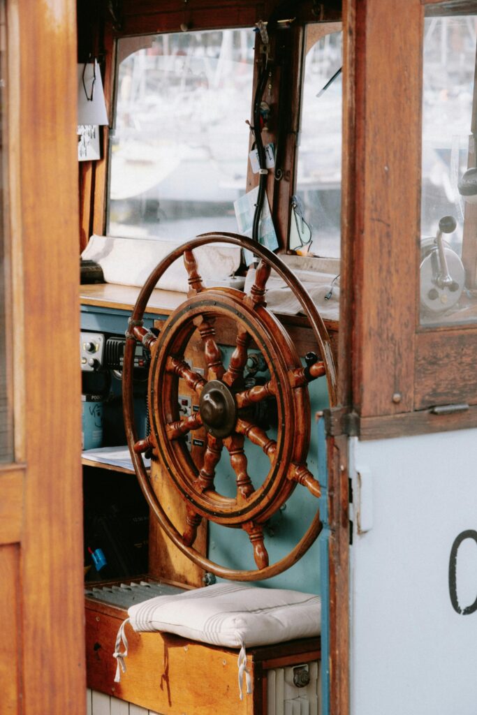 Wooden ship's wheel inside a cozy boat cabin, featuring nautical equipment and a cushioned seat, illustrating a seafaring ambiance.