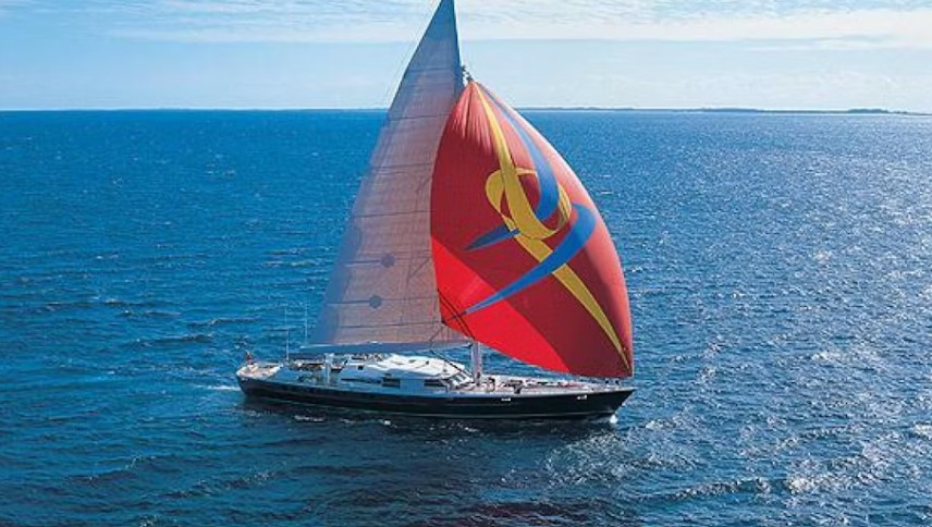 Sailing yacht with a vibrant red and yellow spinnaker glides across a calm, blue ocean under a clear sky, showcasing nautical adventure.