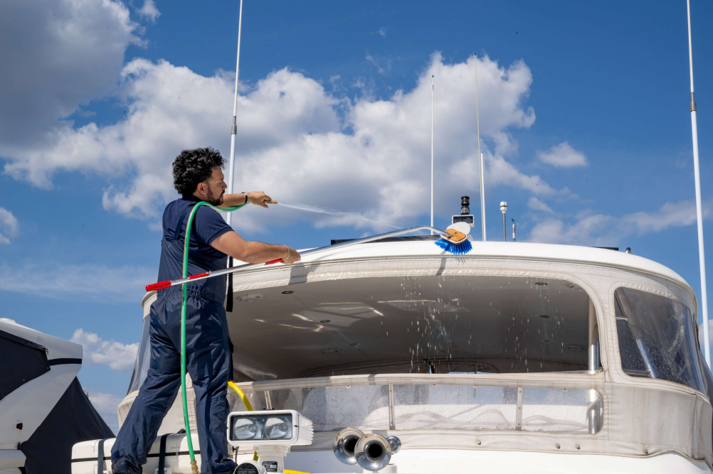 A man cleans the deck of a boat under a blue sky with fluffy clouds, showcasing maintenance and care for watercraft.