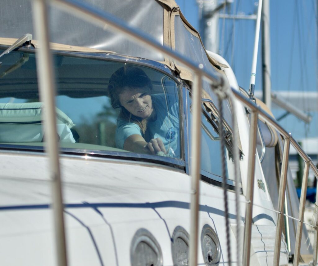 A person carefully cleans the window of a white boat moored at a marina on a sunny day, conveying a sense of focus and tranquility.